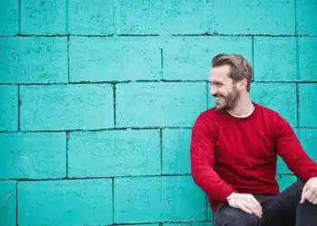 hvad er god ledelse - mand i rød trøje sidder ned ved grøn betonvæg og smiler
