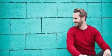 hvad er god ledelse - mand i rød trøje sidder ned ved grøn betonvæg og smiler