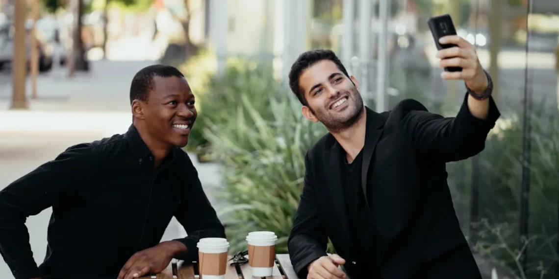 To mænd sidder på cafe og drikker kaffe og tager en selfie som udtryk for den gode samtale