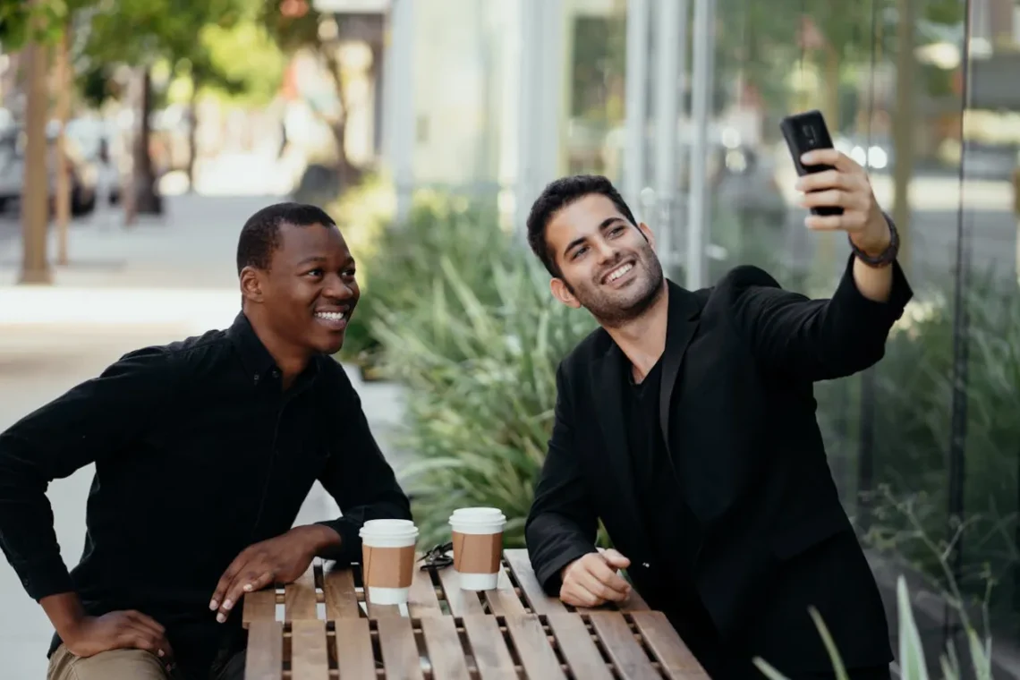 To mænd sidder på cafe og drikker kaffe og tager en selfie som udtryk for den gode samtale