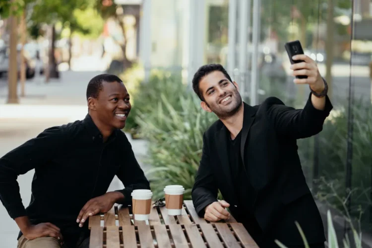 To mænd sidder på cafe og drikker kaffe og tager en selfie som udtryk for den gode samtale