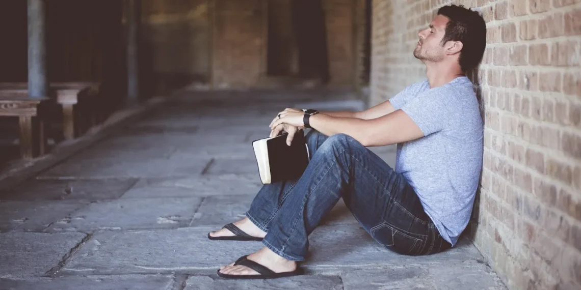 Gaslighting mand sidder alene opad væg med en bog i hånden