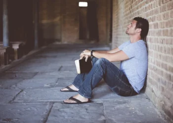 Gaslighting mand sidder alene opad væg med en bog i hånden