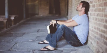 Gaslighting mand sidder alene opad væg med en bog i hånden