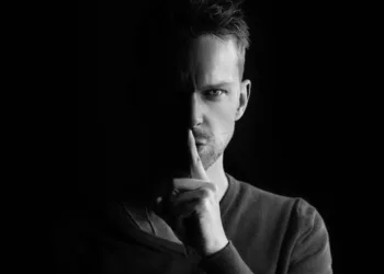 sladder og gossip på arbejdspladsen - mand holder pegefingeren op for munden shh