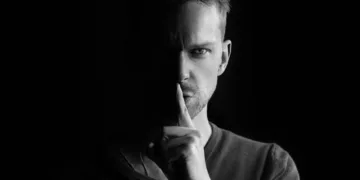 sladder og gossip på arbejdspladsen - mand holder pegefingeren op for munden shh