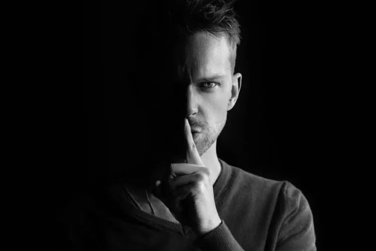 sladder og gossip på arbejdspladsen - mand holder pegefingeren op for munden shh