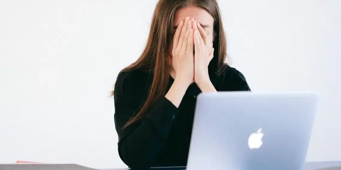 stress symptomer - kvinde begraver ansigtet i hænderne foran MacBook computer