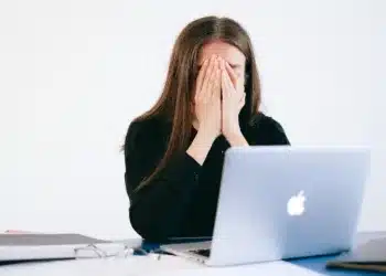 stress symptomer - kvinde begraver ansigtet i hænderne foran MacBook computer