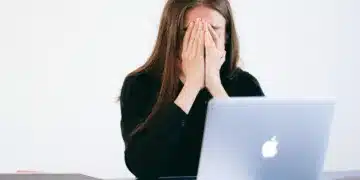 stress symptomer - kvinde begraver ansigtet i hænderne foran MacBook computer