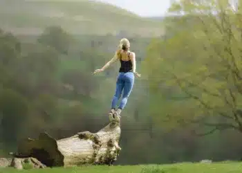 Herzbergs to-faktor teori - kvinde står på træstamme og strækker sig mod himlen