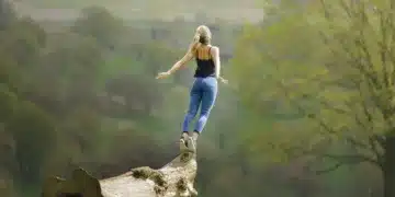 Herzbergs to-faktor teori - kvinde står på træstamme og strækker sig mod himlen