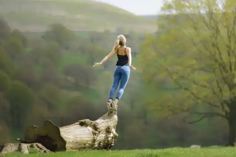 Herzbergs to-faktor teori - kvinde står på træstamme og strækker sig mod himlen