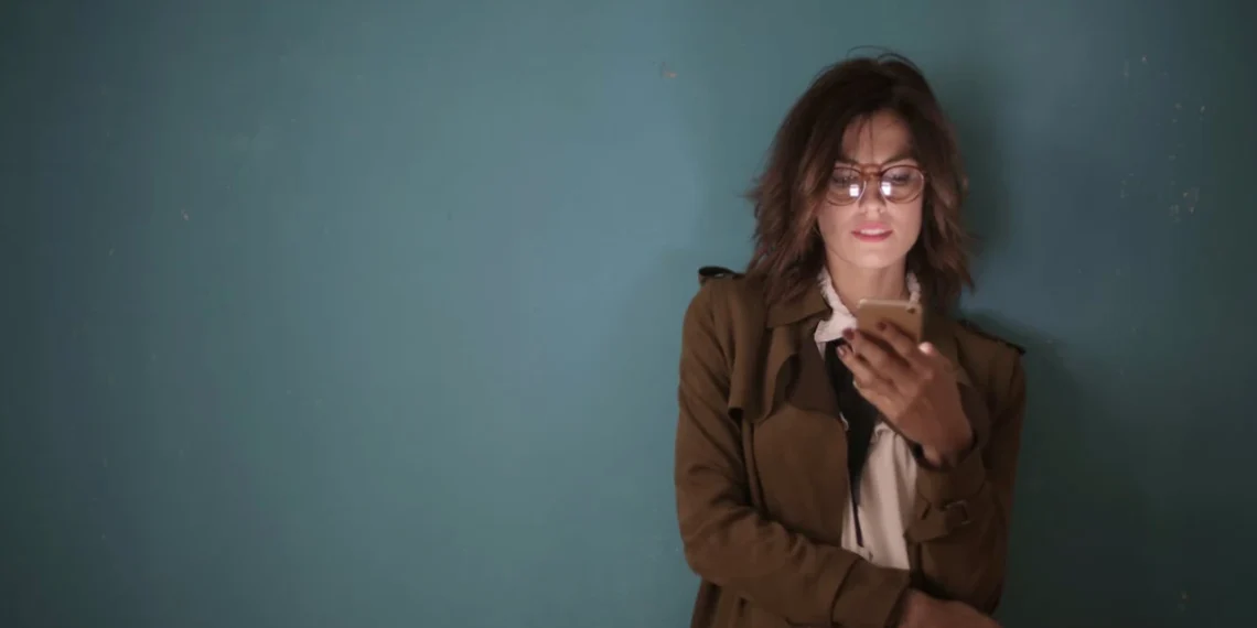 Kvinde står opad væg med mobiltelefon i hånden som synonym for TEAL