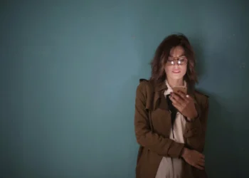 Kvinde står opad væg med mobiltelefon i hånden som synonym for TEAL