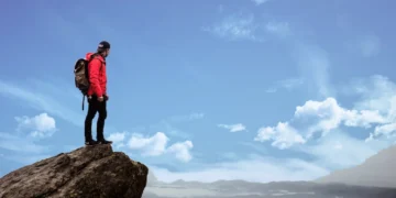 Motivationsfaktorer - mand står på toppen af bjerg helt oppe i skyerne