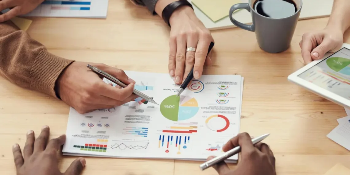 6 hænder oppefra. En hånd peger på regnskabspapir som i økonomistyring oekonomistyring