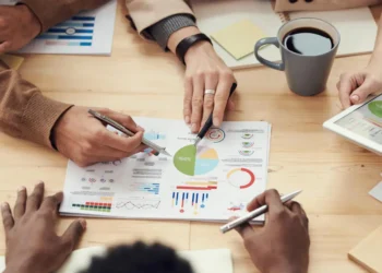 6 hænder oppefra. En hånd peger på regnskabspapir som i økonomistyring oekonomistyring