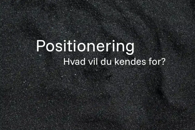 Positionering skrevet med hvid tekst på strand med sorte sandkorn