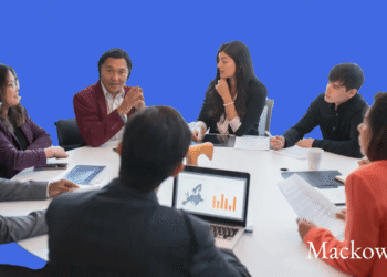 Syv mennesker sidder om rundt bord som i teamwork