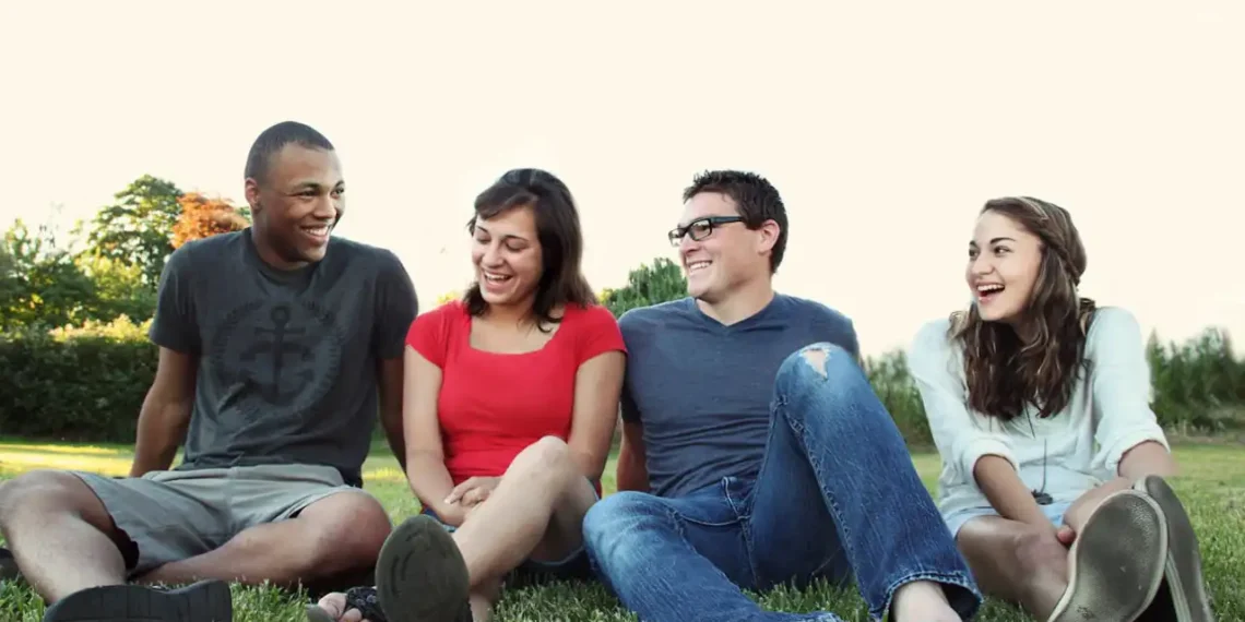 4 mennesker sidder på græsplæne og smiler som i inklusion.