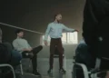 Mand står i sportshal med kreds af mennesker som i coaching.