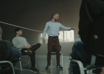 Mand står i sportshal med kreds af mennesker som i coaching.