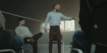 Mand står i sportshal med kreds af mennesker som i coaching.