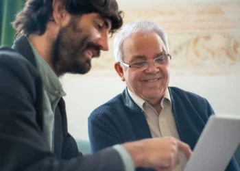 Yngre medarbejder sidder med ældre mentor ved computer.