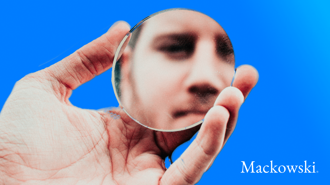 Hånd holder rundt spejl med spejlbillede af mand som selvindsigt